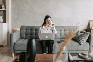 Jak przygotować się do urlopu w biznesie online? Kobieta siedzi na kanapie i ustawia wiadomości urlopowe na komputerze.